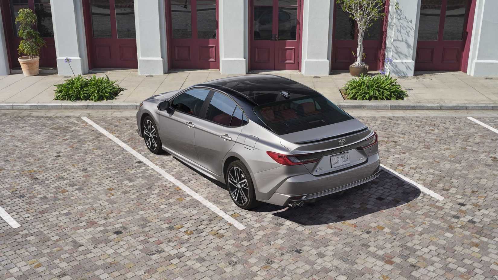 Foto traseira 3/4 de um Toyota Camry XSE 2025 cinza estacionado do lado de fora de um prédio.