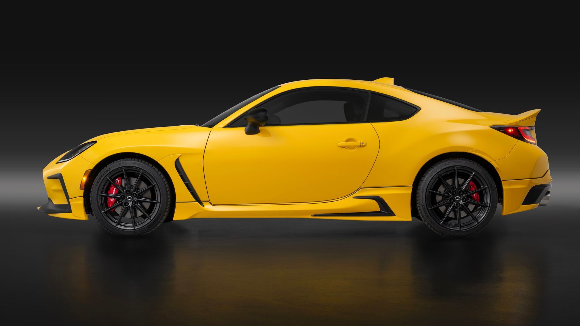 Side profile photo of a yellow Toyota GR86 Yuzu 2026 in a studio against a black background.