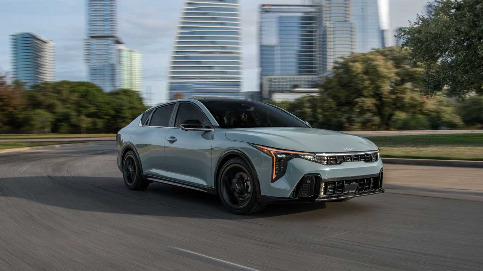 Front 3/4 view of a gray 2025 Kia K4 driving through a city.