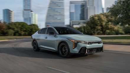 Front 3/4 view of a gray 2025 Kia K4 driving through a city.