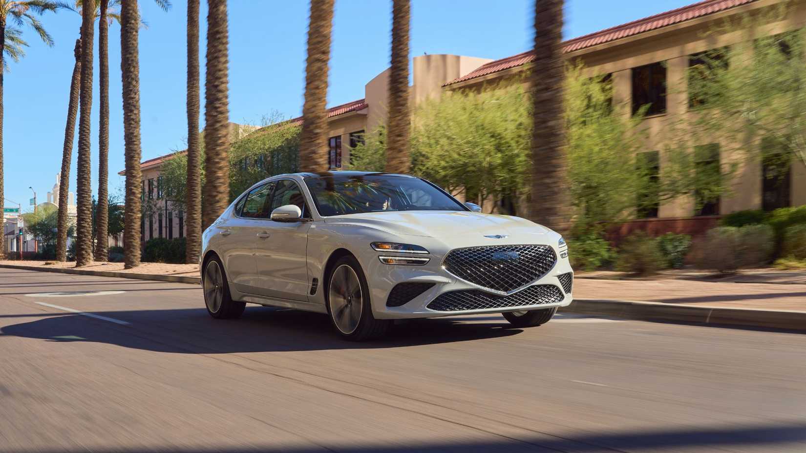Front 3/4 shot of a gray 2025 Genesis G70 driving through a city with palm trees lining the road.