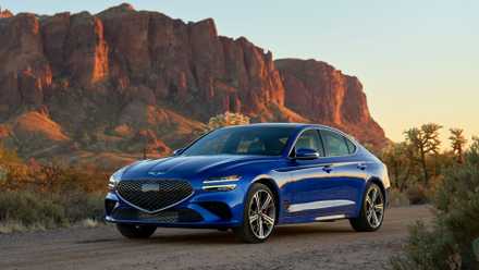 Front 3/4 shot of a blue 2025 Genesis G70 parked on gravel with a mountain in the background.