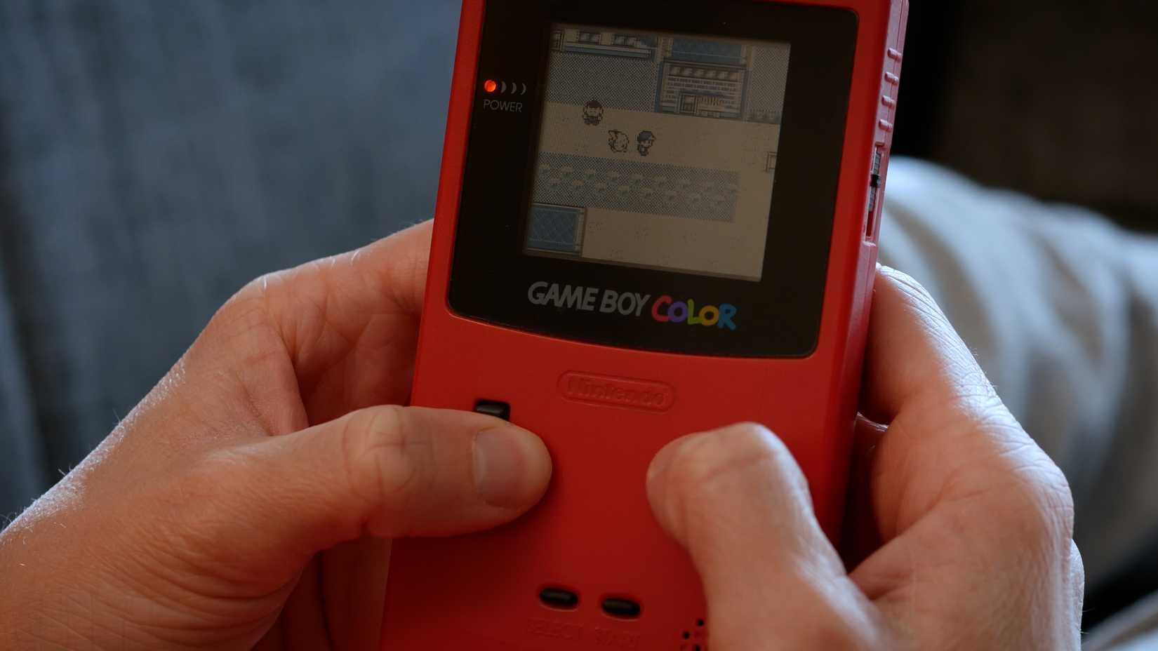 A person playing Pokemon on a Game Boy Color.