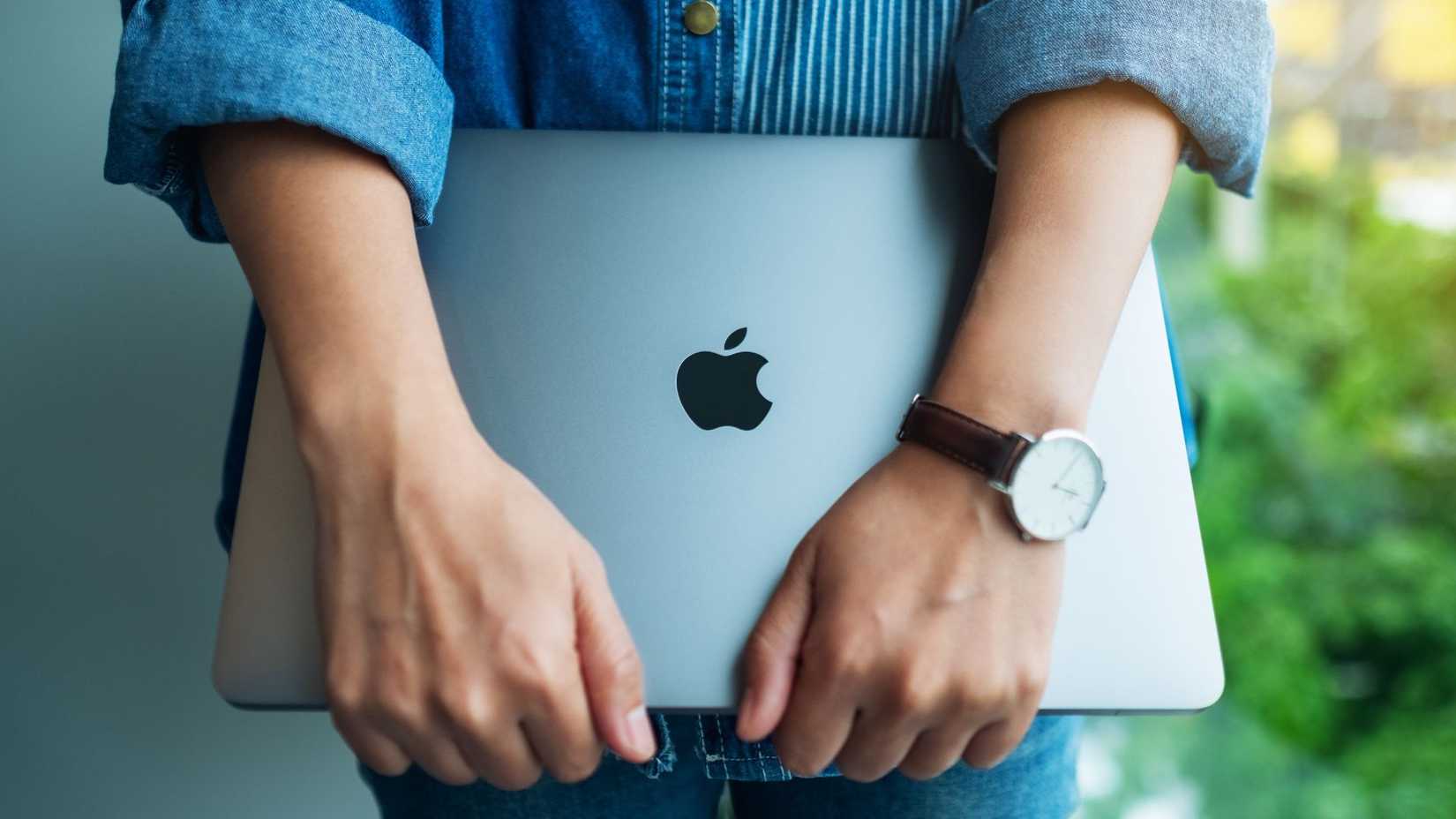 A woman standing and holding an Apple MacBook Pro laptop.