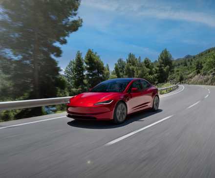 Front 3/4 shot of a red 2024 Tesla Model 3 driving on a winding country road.