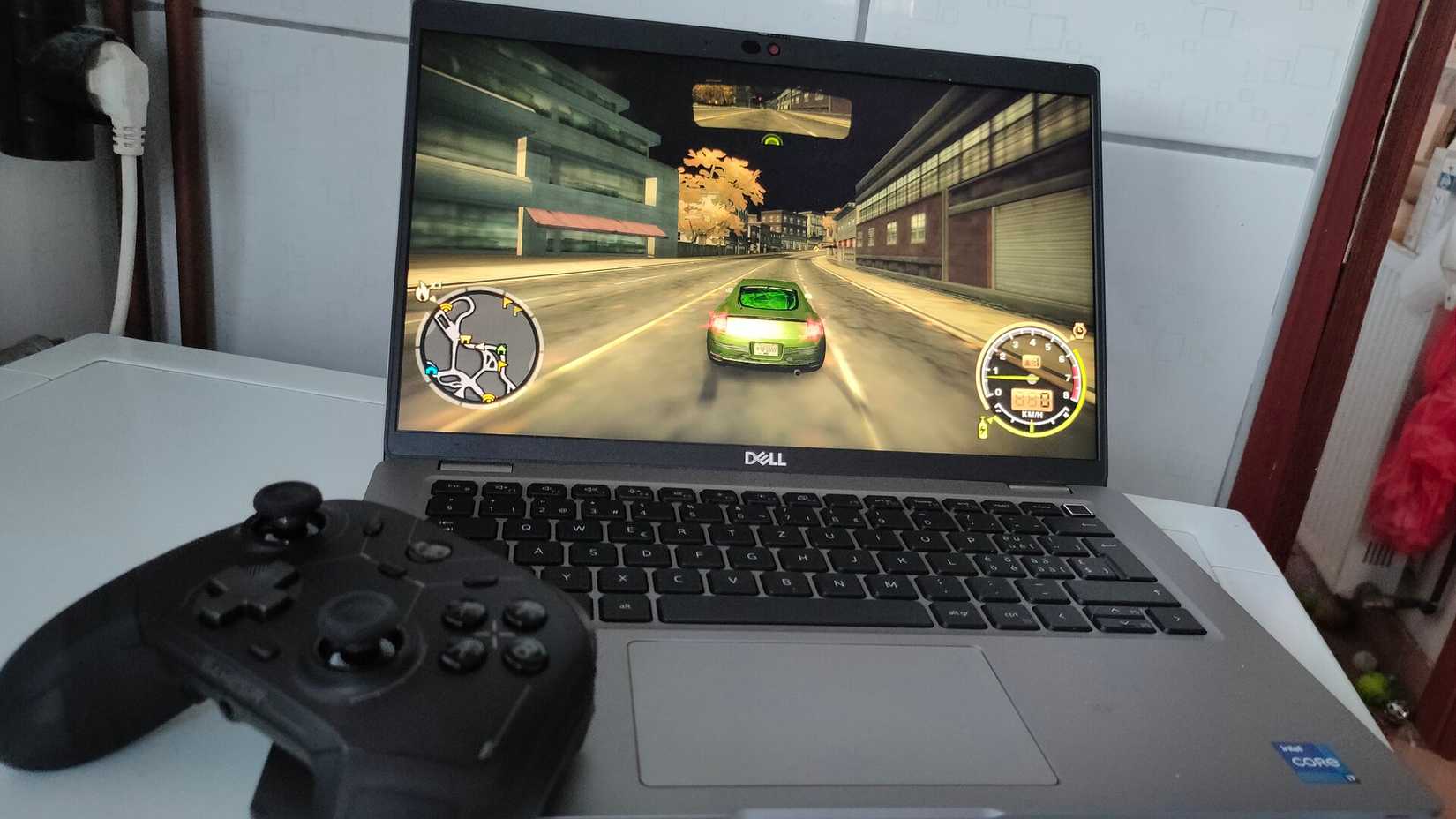 A Dell Latitude 5420 business laptop running "Need For Speed Most Wanted" with a black controller on top of its keyboard.