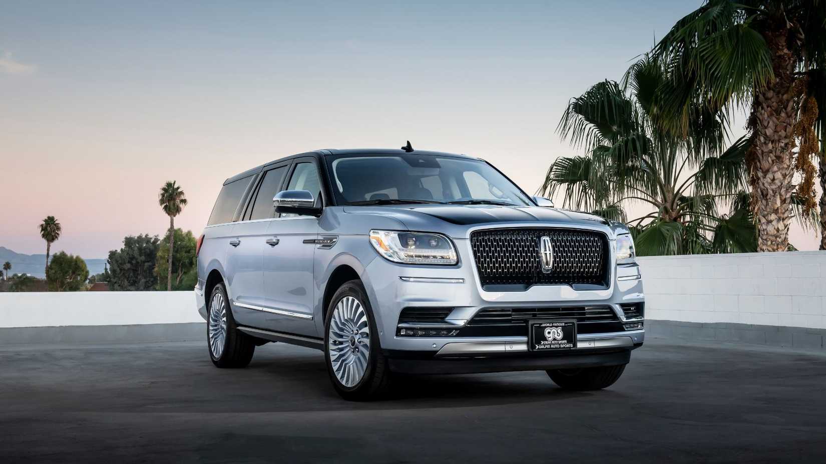 Front 3/4 shot of a silver 2018 Lincoln Navigator parked on tarmac with palm trees in the background.