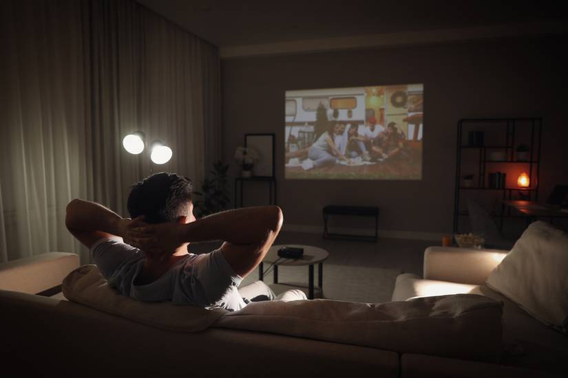 A man watching a movie on the sofa with the room mostly in darkness.