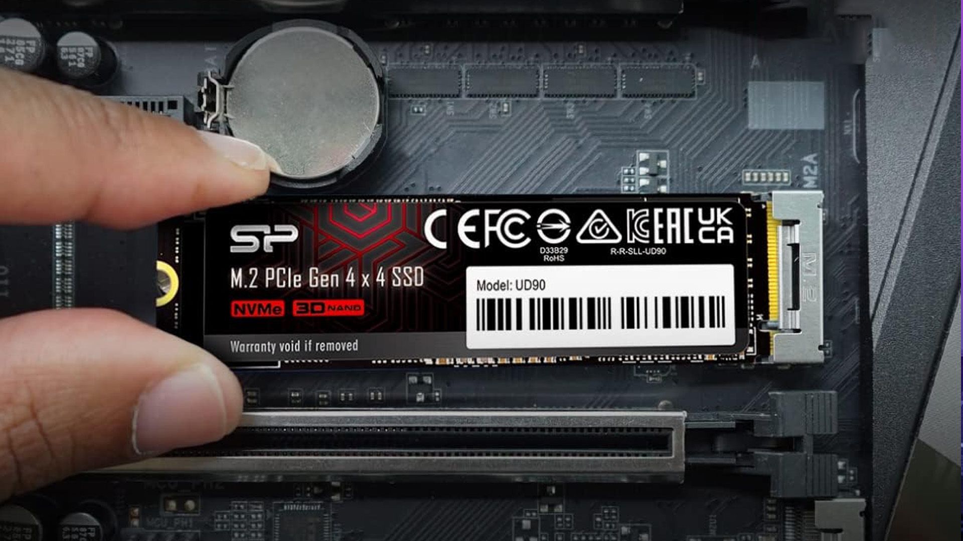 A hand installing the Silicon Power UD90 2TB NVMe SSD into a motherboard.