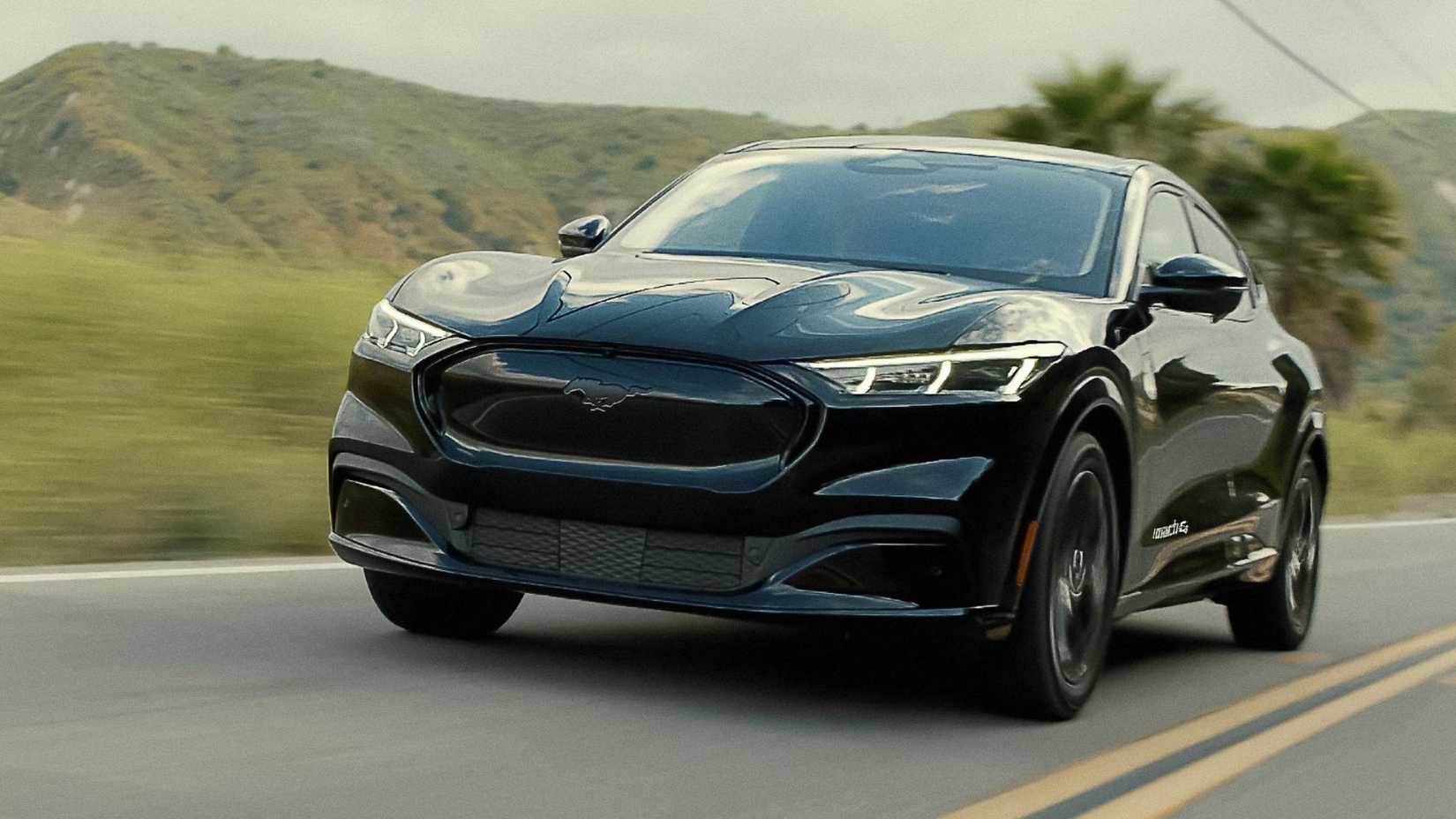 Tiro dinámico de 3/4 del frente de un Mustang Mach-E Premium 2023 negro conduciendo por una carretera rural.