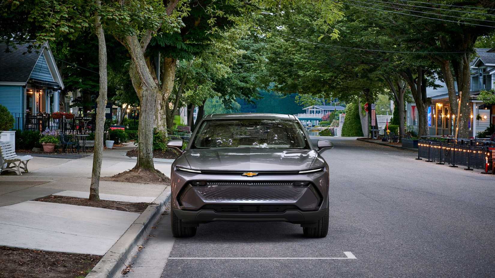 Static shot of the front of a gray 2024 Chevrolet Equinox EV 1LT parked along a sidewalk in a residential neighborhood.
