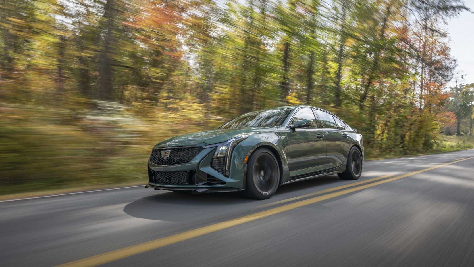 A dynamic 3/4 front shot of a green 2025 Cadillac CT5-V Blackwing driving down a country road.
