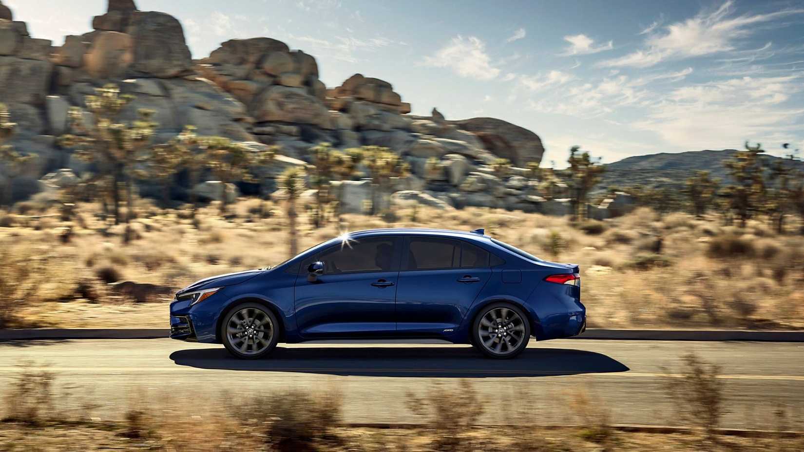 Dynamic side profile shot of a blue 2025 Toyota Corolla Hybrid driving on a country road through the desert.