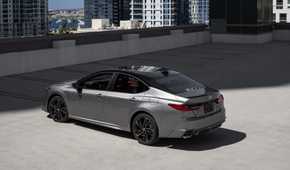 Static rear 3/4 shot of a gray 2025 Toyota Camry XSE AWD parked with highrise buildings in the background.
