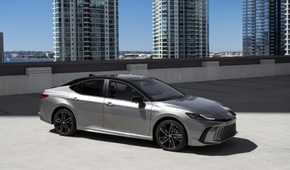 Static side profile shot of a gray 2025 Toyota Camry XSE AWD parked with highrise buildings in the background.