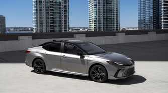 Static side profile shot of a gray 2025 Toyota Camry XSE AWD parked with highrise buildings in the background.