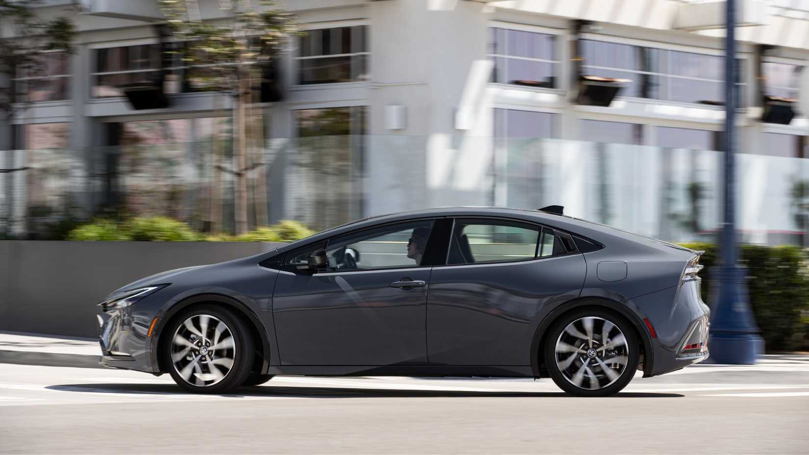 Dynamic side profile shot of a gray 2025 Toyota Prius PHEV XSE Premium driving in a city.