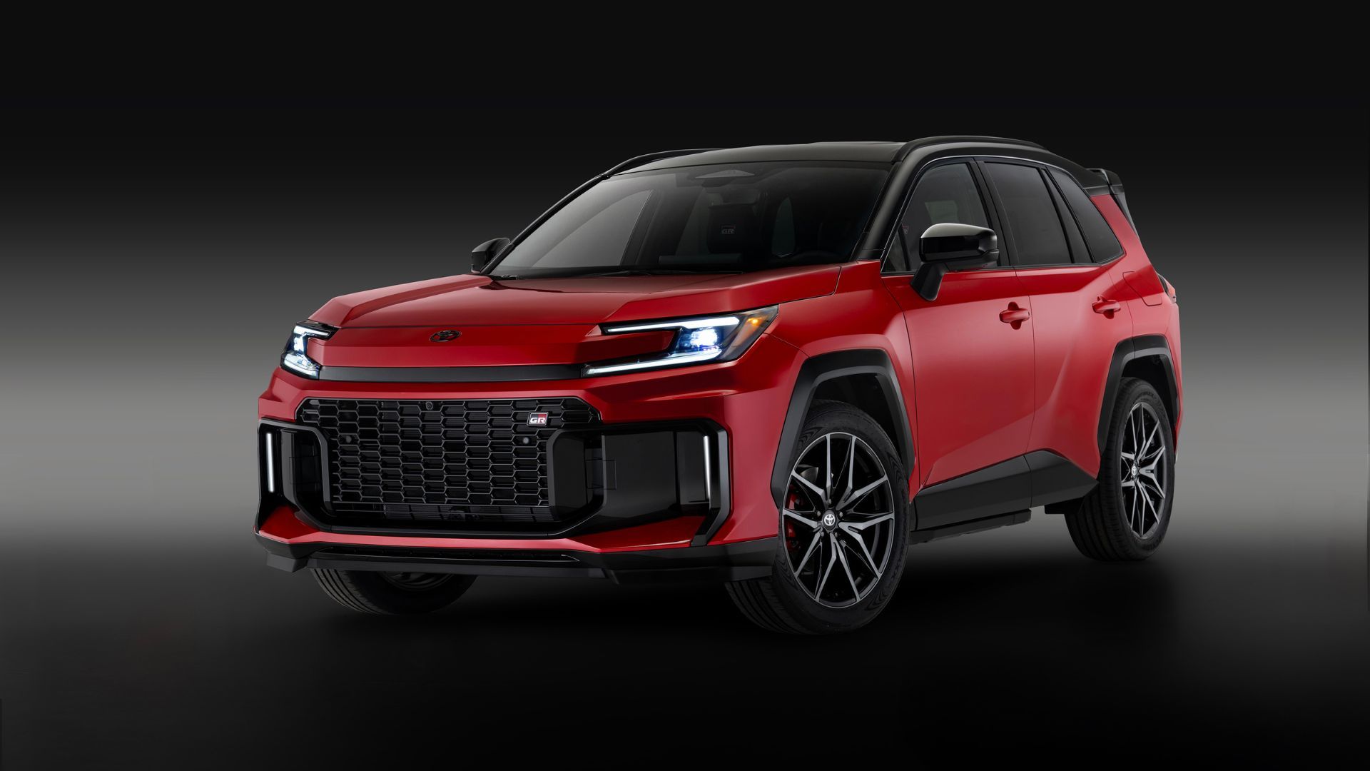 Static front 3/4 shot of a red 2026 Toyota RAV4 PHEV GR Sport in a studio with a black and gray backdrop.