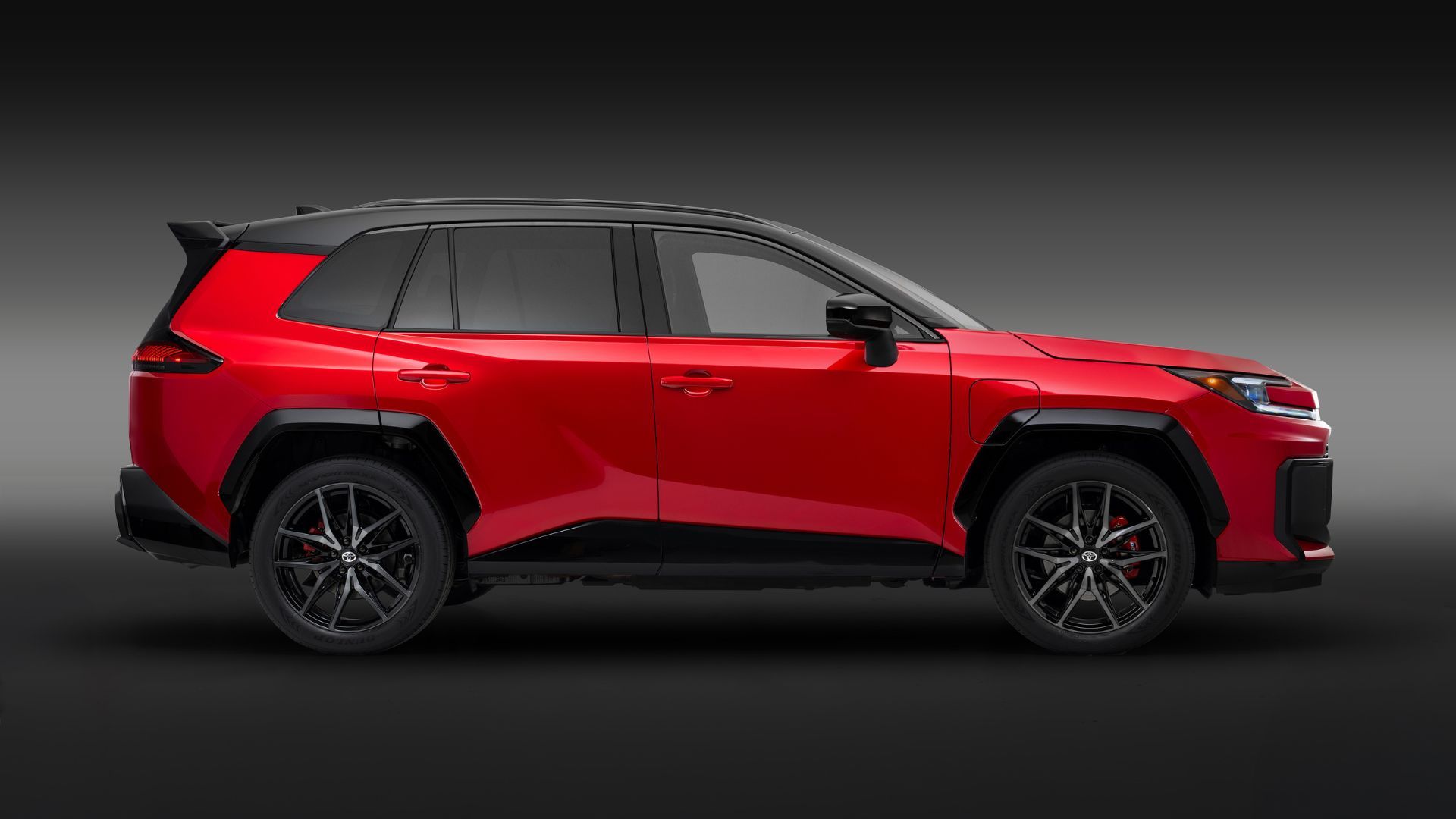 Static side profile shot of a red 2026 Toyota RAV4 PHEV GR Sport in a studio with a black and gray backdrop.