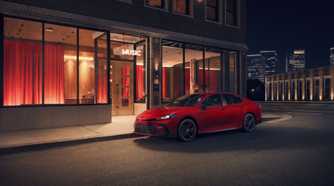 Static front 3/4 shot of a red 2026 Toyota Camry Nightshade parked outside of a building.
