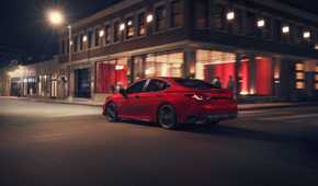 Dynamic rear 3/4 shot of a red 2026 Toyota Camry Nightshade driving through a city.