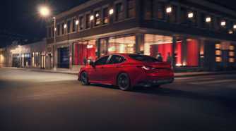 Dynamic rear 3/4 shot of a red 2026 Toyota Camry Nightshade driving through a city.