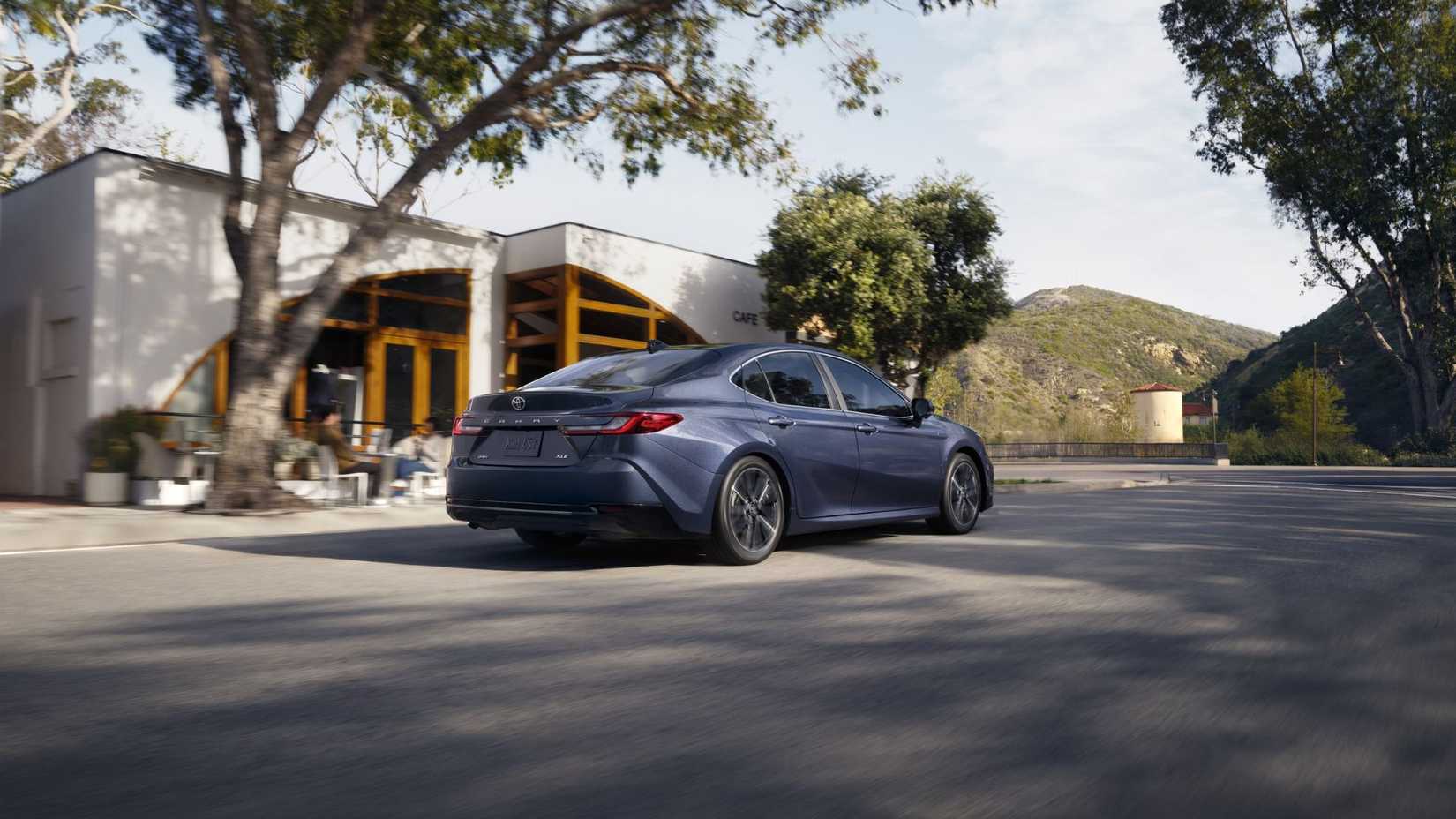 Dynamic rear 3/4 shot of a gray 2026 Toyota Camry driving through a city.