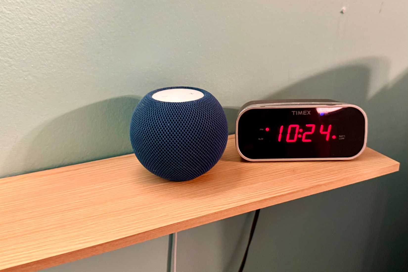 HomePod mini em uma prateleira ao lado de um relógio digital.