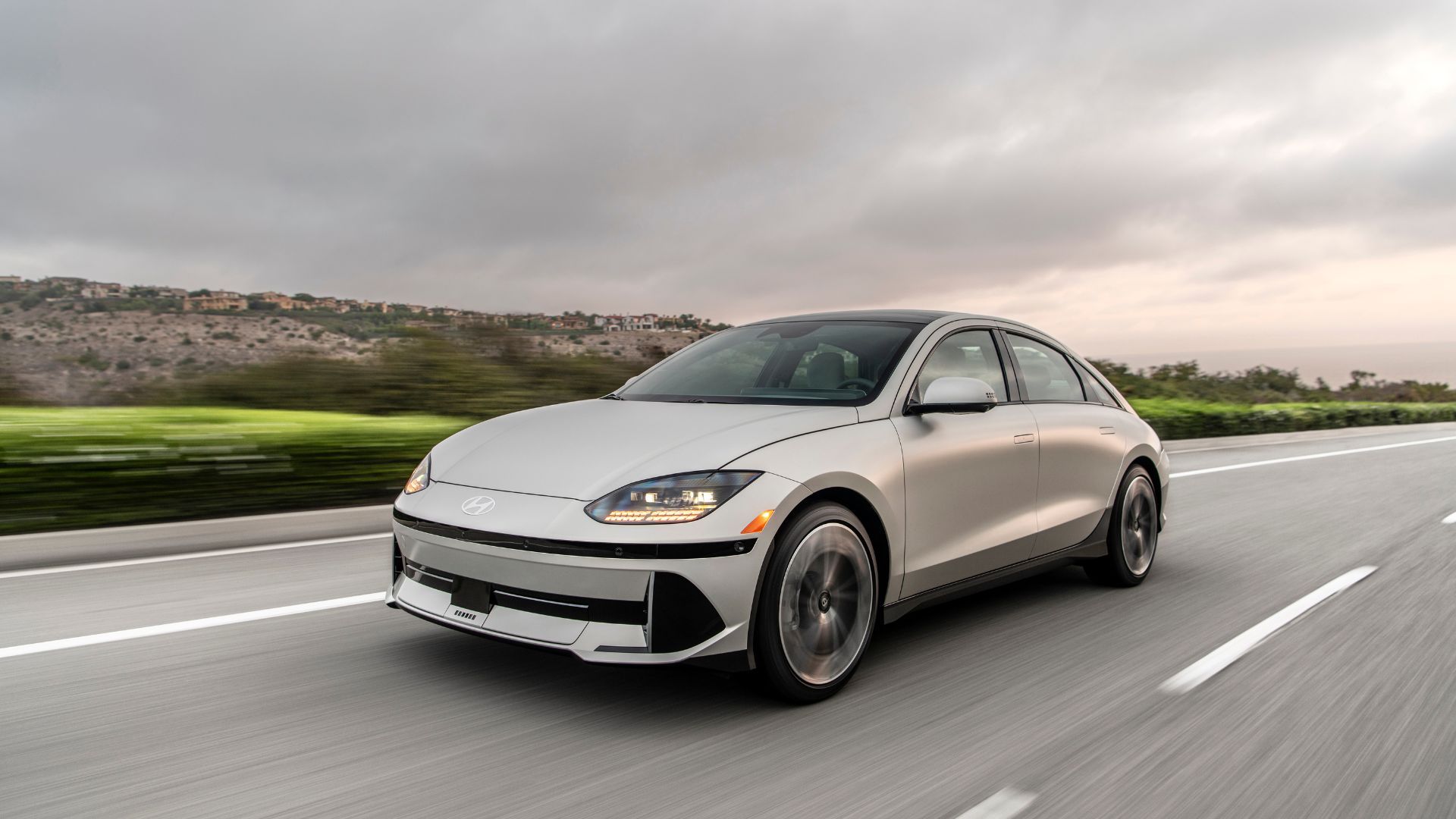 Dynamic front 3/4 shot of a silver 2025 Hyundai Ioniq 6 driving on a country road.