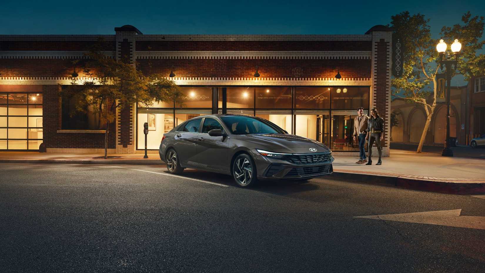 Static front 3/4 shot of a gray 2026 Hyundai Elantra Hybrid palkred outside of a store.