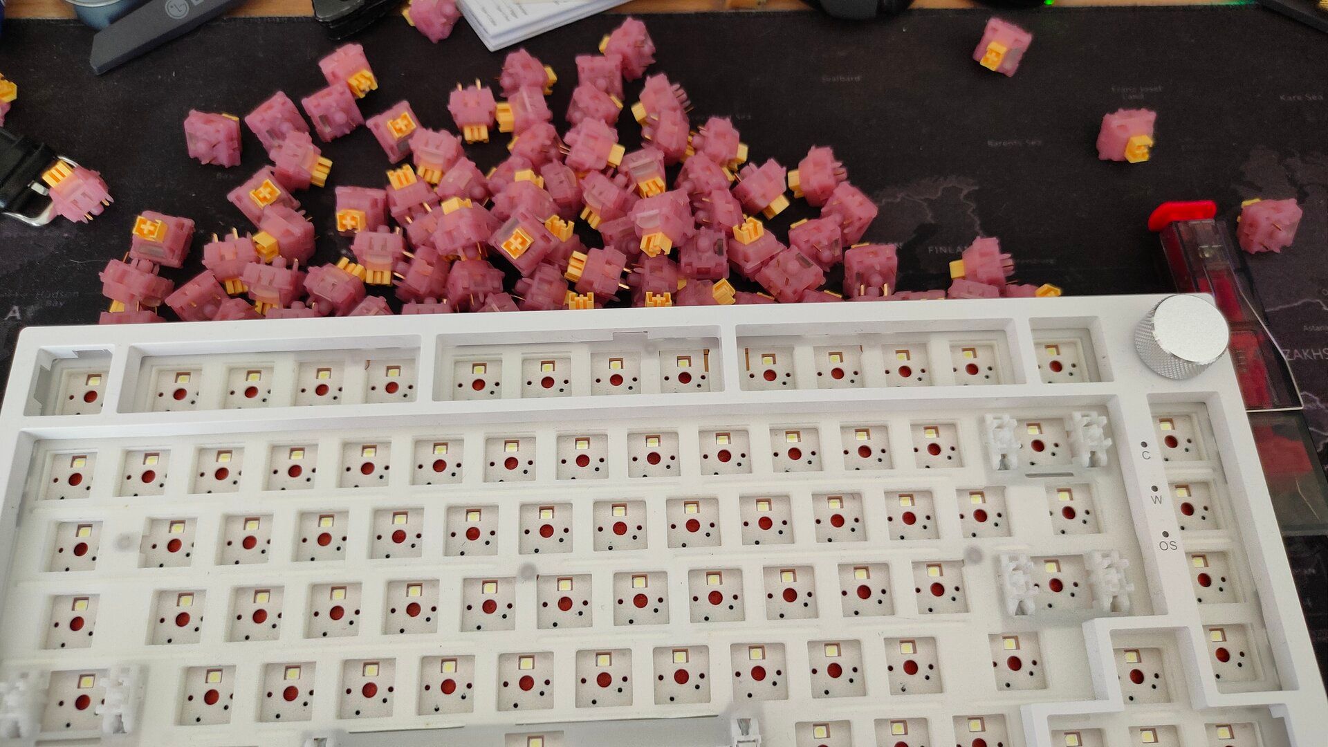 A barebones mechanical keyboard with all the switches removed and pink switches above it.