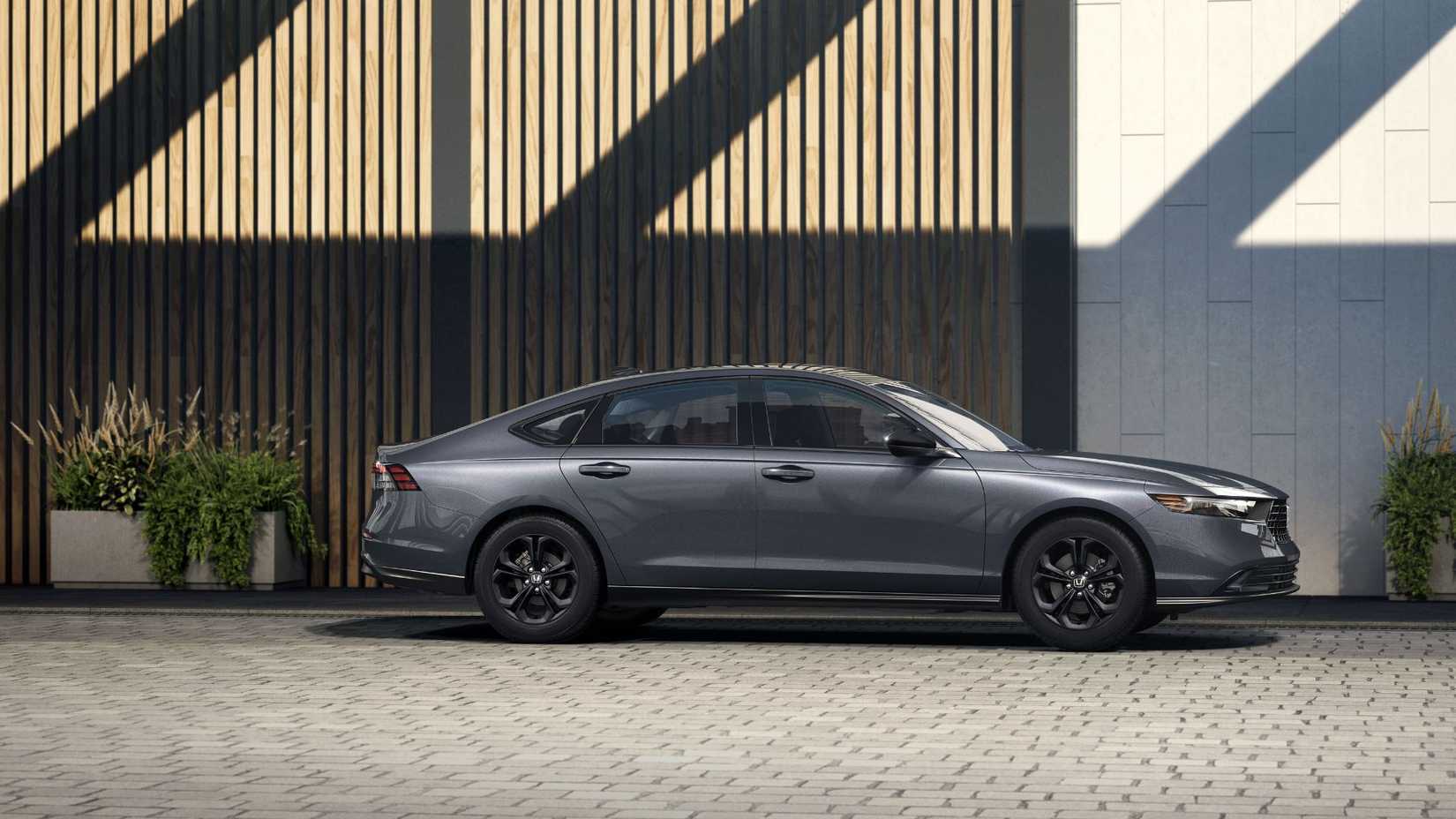 Static side profile shot of a gray 2025 Honda Accord SE parked outside of a modern building.
