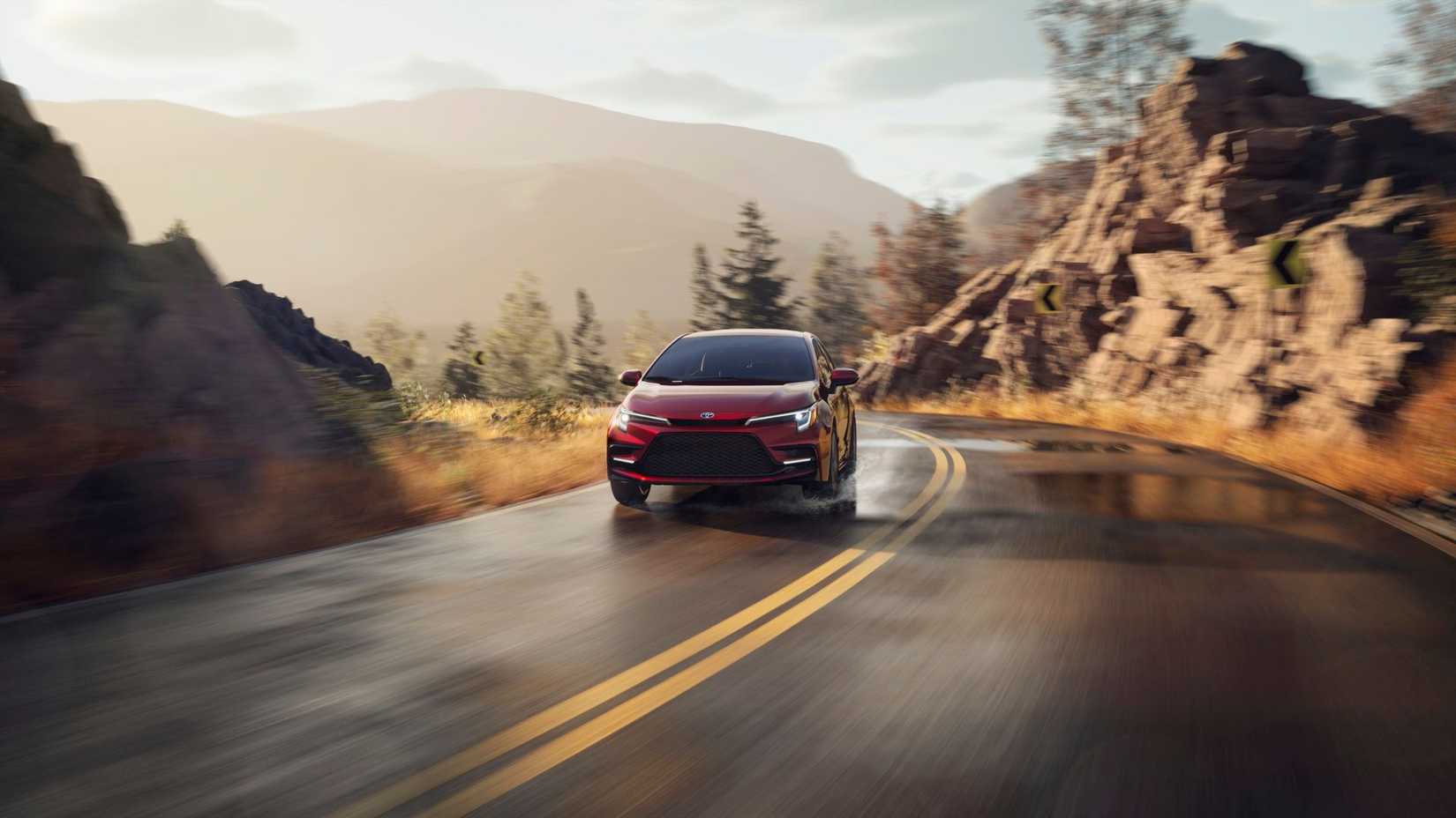Dynamic front end shot of a red 2025 Toyota Corolla Hybrid driving on a wet country road through the mountains.