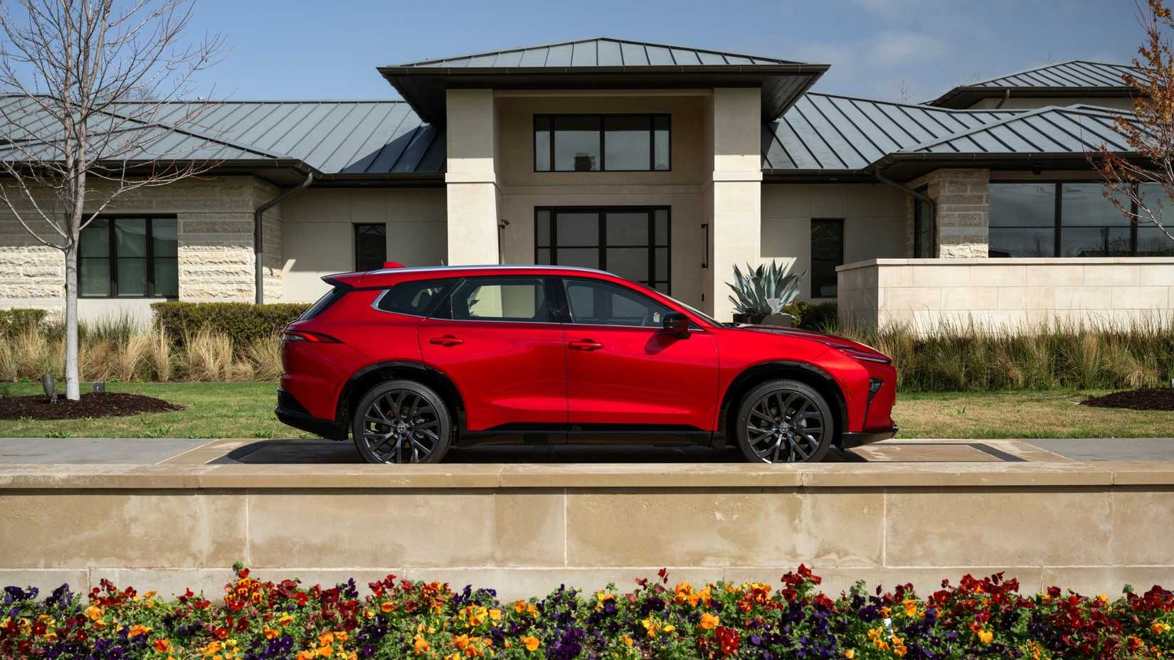 A static side profile shot of a red 2025 Toyota Crown Signia Limited parked outside a house.