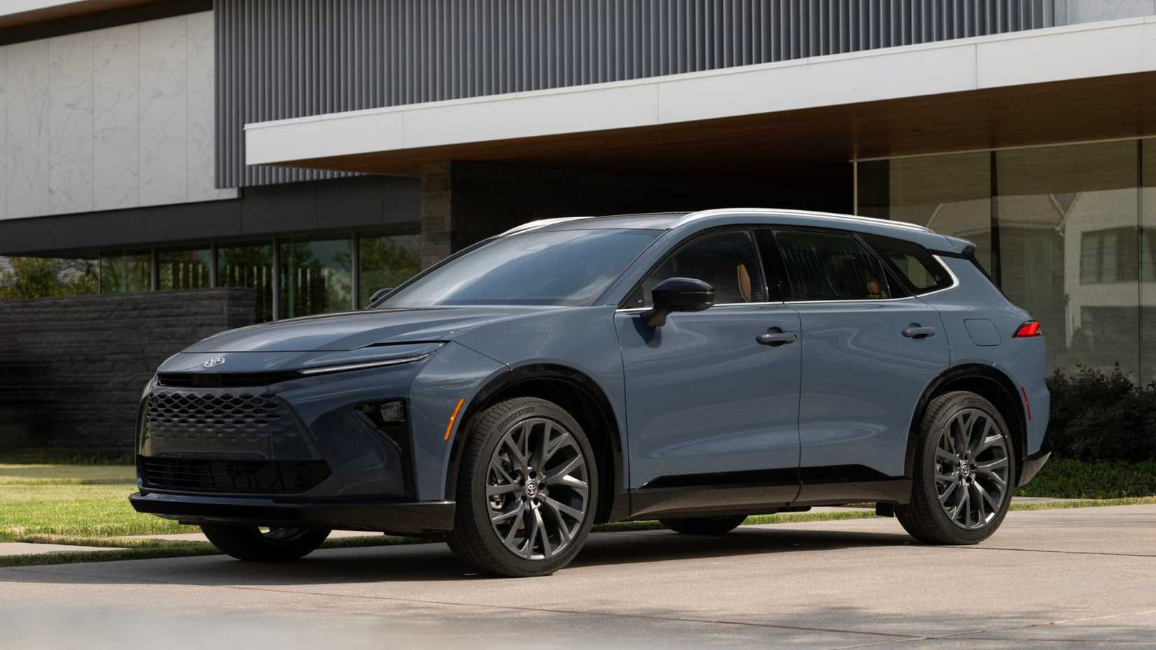 モダンな建物の外に駐車されているグレーの 2025 トヨタ クラウン シグニア リミテッドの静止フロント 3/4 ショット。