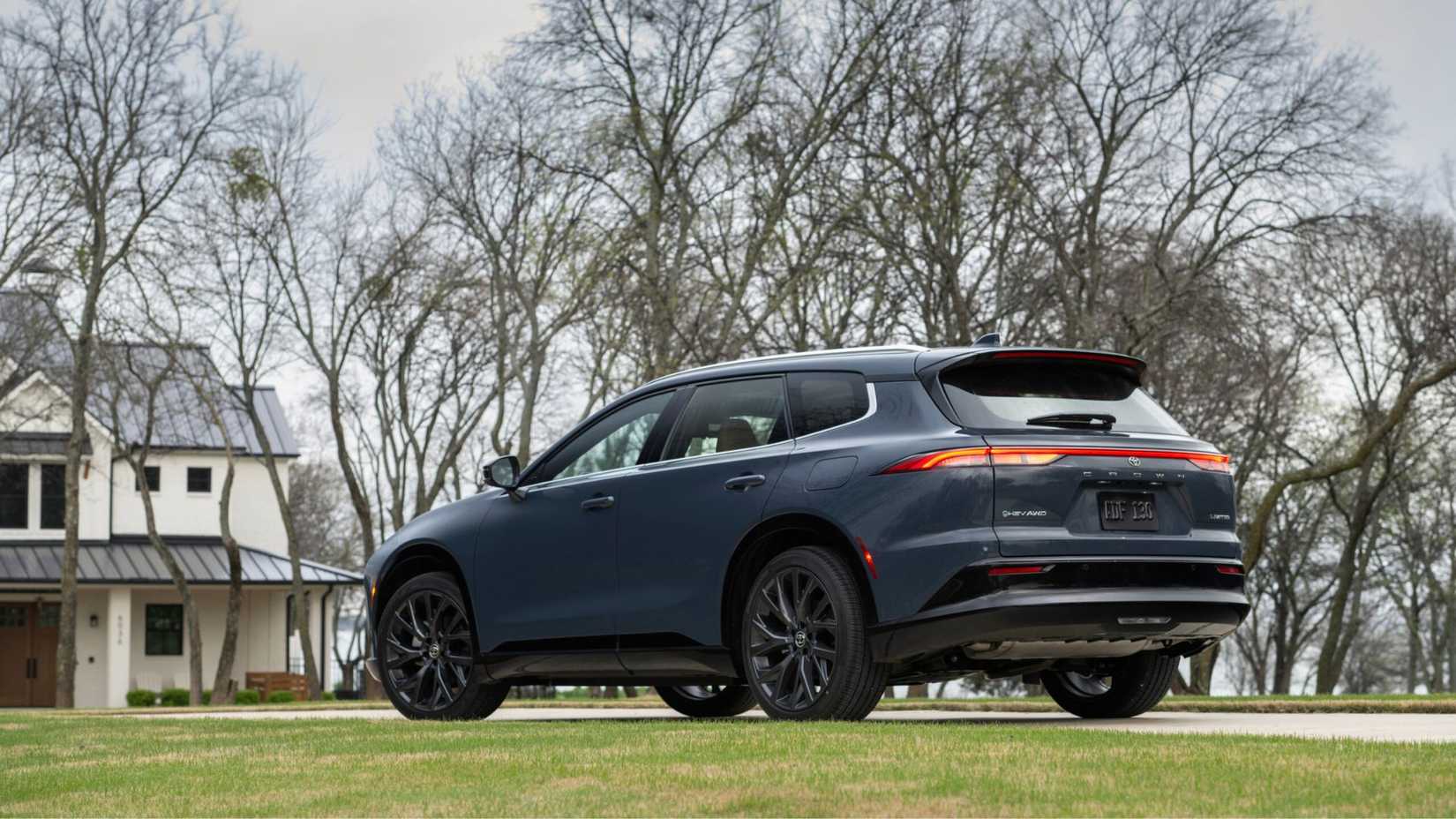 Static rear 3/4 shot of a gray 2025 Toyota Crown Signia Limited parked on the driveway outside of a house with trees in the background.