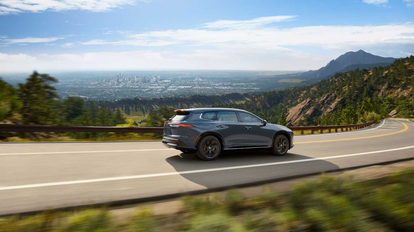 Dynamic side profile shot of a gray 2025 Toyota Crown Signia driving on a country road through the mountains with a city in the distance.