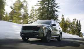 Dynamic front 3/4 shot of a 2026 Kia Sorento driving on a snow-lined country road.