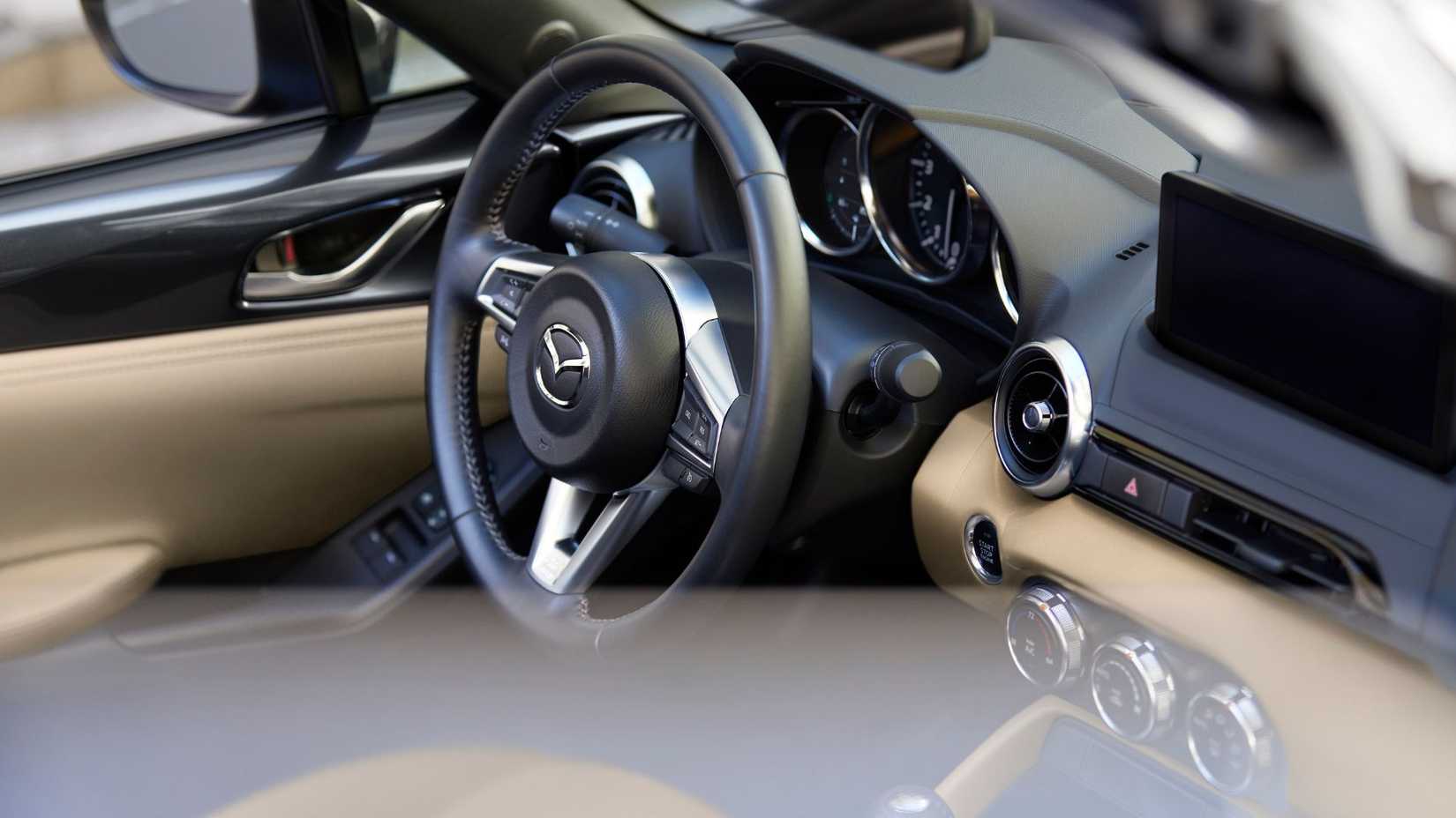 Close-up shot of the interior of a 2024 Mazda MX-5, showing the steering wheel, infotainment screen, and cream leather.