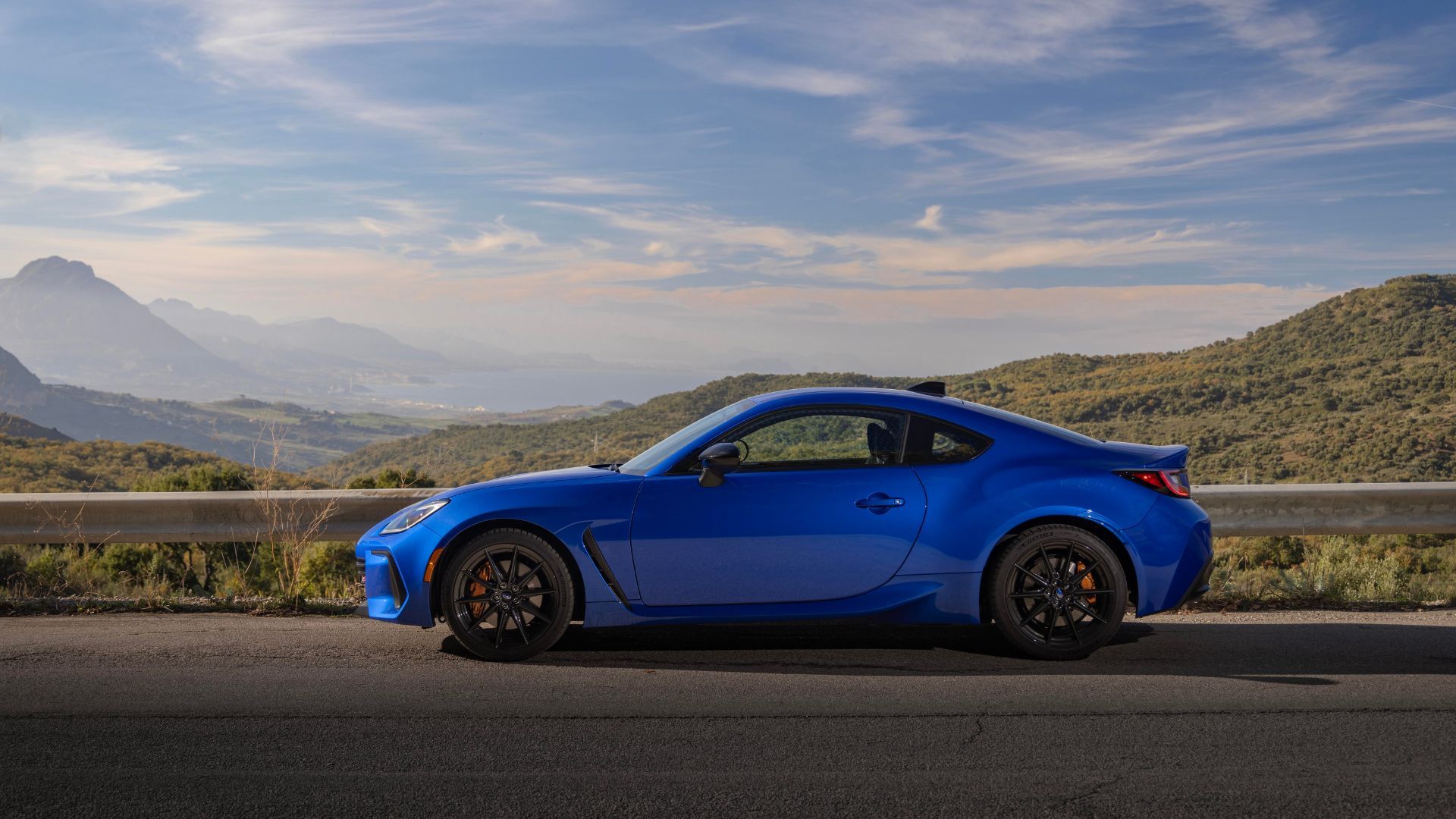 Photo de profil latérale statique d'une Subaru BRZ tS 2024 bleue avec des montagnes et des arbres en arrière-plan.