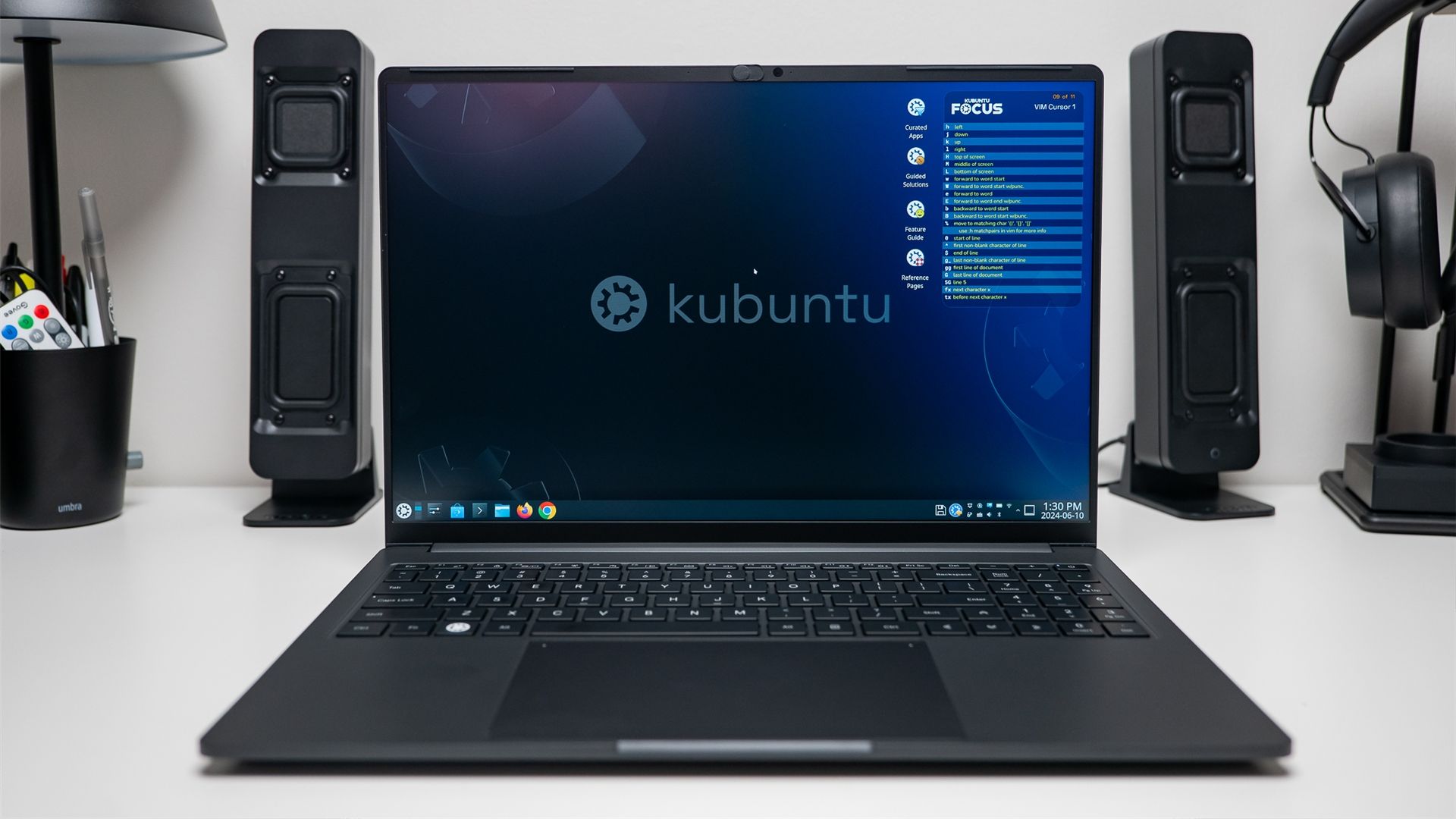 A laptop running Kubuntu on a white desk with speakers. 