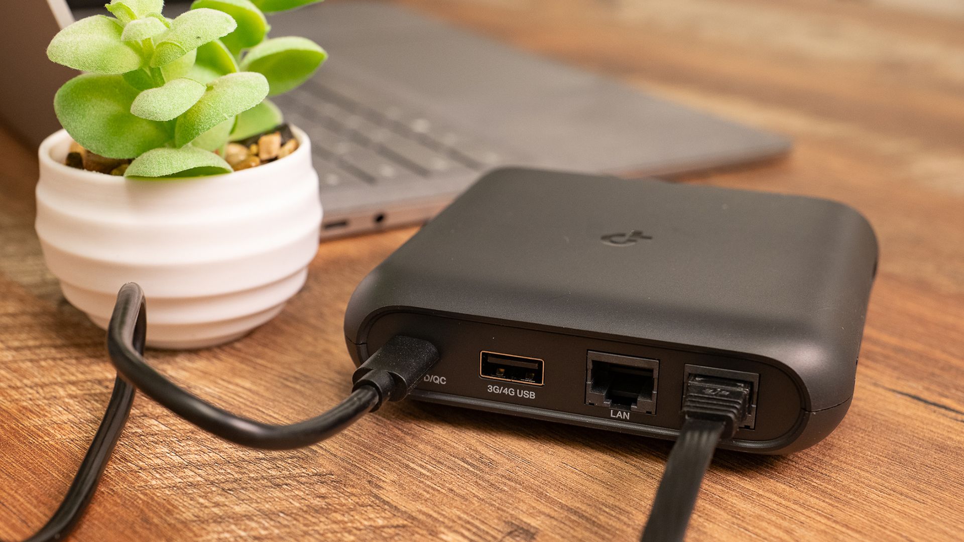 A travel router next to a laptop and little plant. 