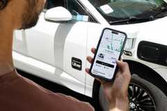 A man looking at his Uber app next to a car with the Uber logo on it.