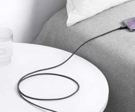 Anker USB C to USB C Cable hung over a night stand next to a bed, charging a phone.
