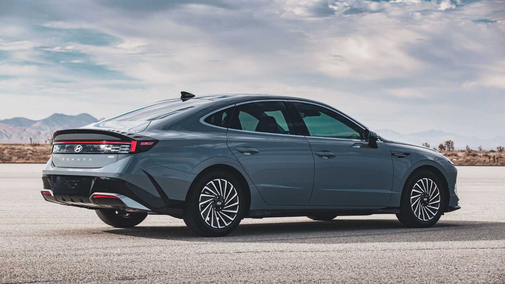Static rear 3/4 shot of a gray 2025 Hyundai Sonata Hybrid Limited parked on tarmac with mountains in the background.