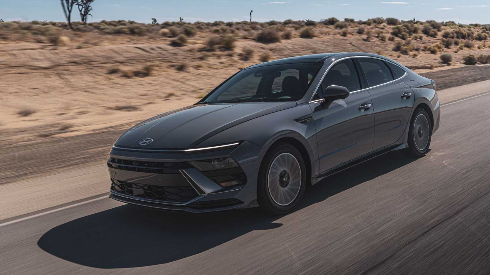 Dynamic front 3/4 shot of a gray 2025 Hyundai Sonata Hybrid Limited driving on a country road.