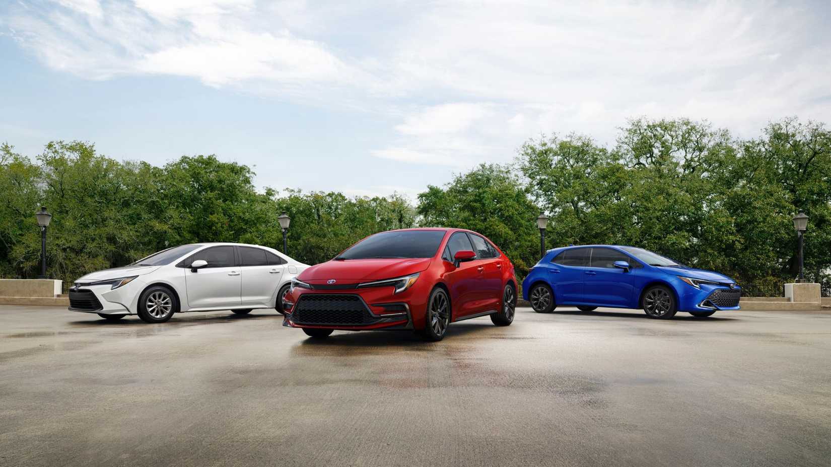 Shot of a red 2023 Toyota Corolla Hybrid parked in between two other Toyota models with trees in the background.