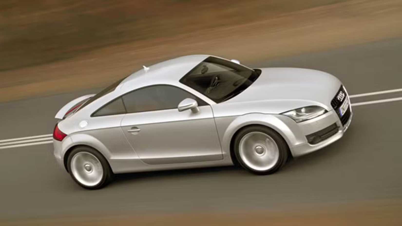 Dynamic side profile shot of a silver 2009 Audi TT 3.2 Quattro driving on a country road.