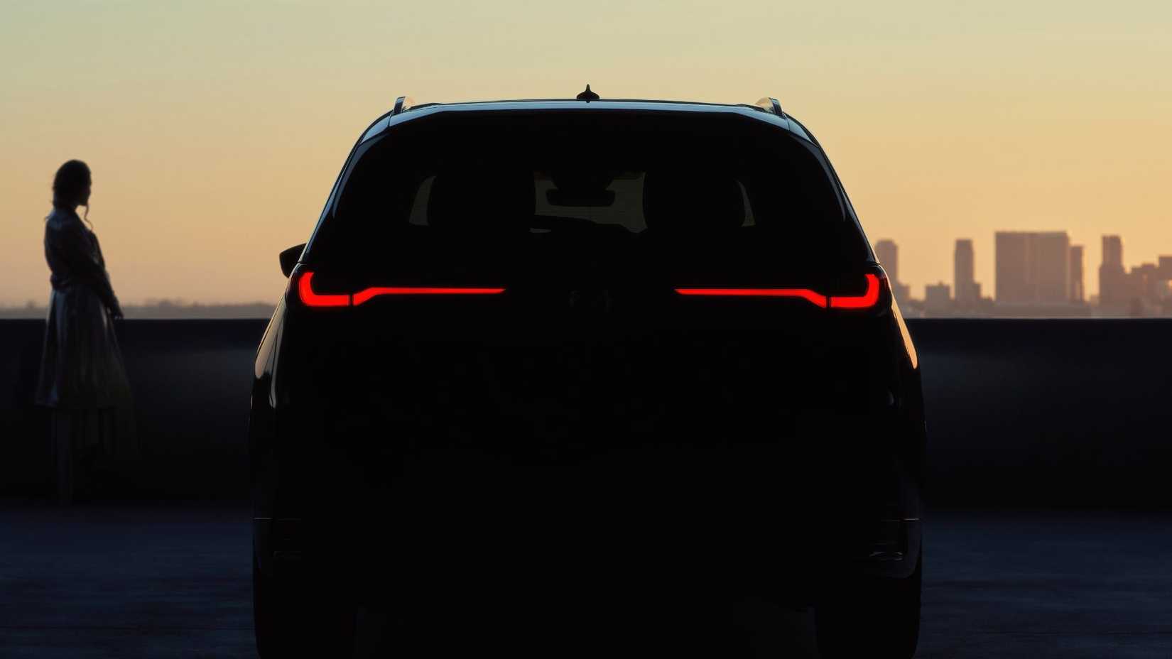 Static rear-end shot of a 2026 Mazda CX-90 parked in shadows with a cityscape in the ‍background.