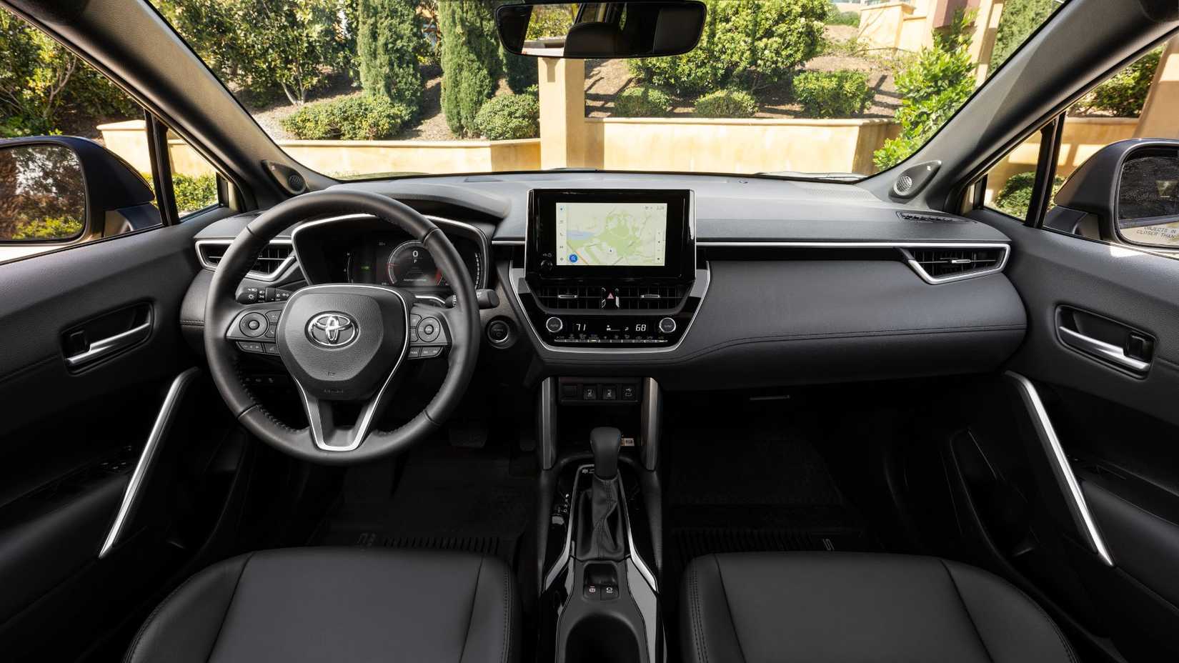 Shot inside the cabin of a 2024 Toyota Corolla Cross Hybrid XSE, showing the front seats, steering wheel, and infotainment screen.